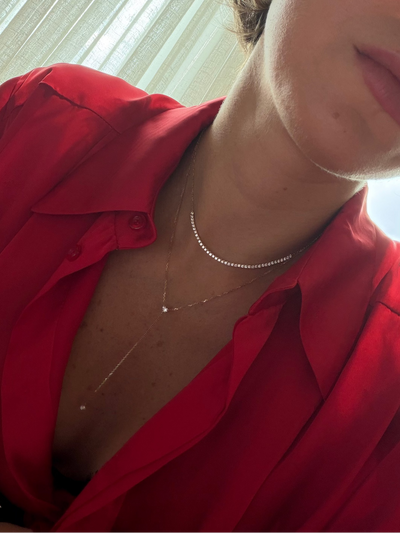 Woman wearing a red silky shirt with a stack of simple diamond necklaces, close-up of neck and chest area.